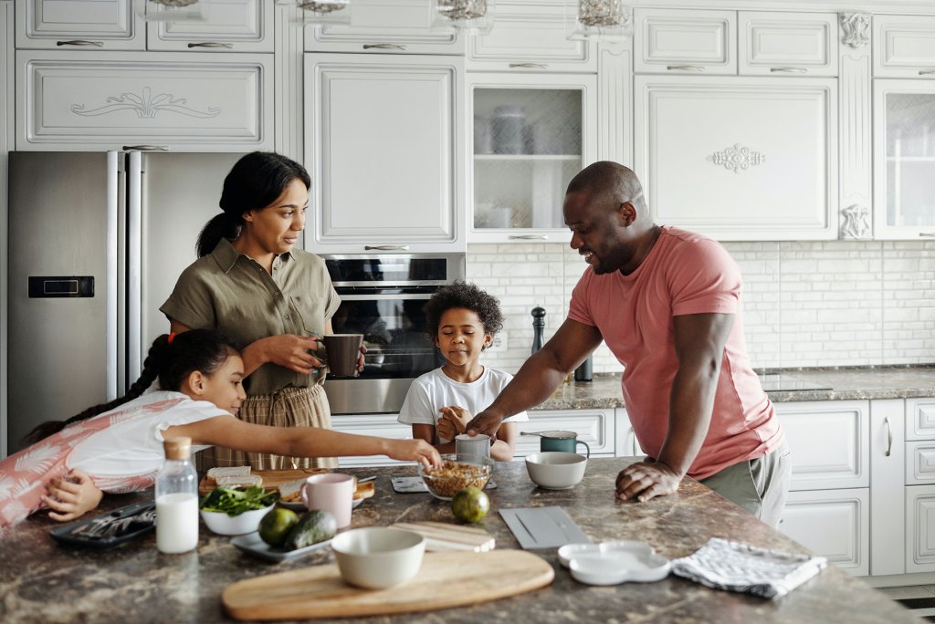 Happy family eating together in a bright kitchen. Picture by Pexels.